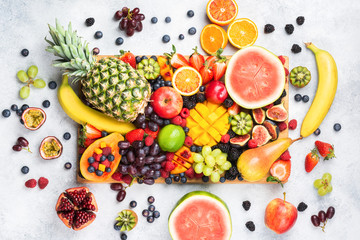 Healthy raw rainbow fruit platter background, mango papaya strawberries oranges blueberries pineapple watermelon on wooden board on light concrete background, top view, selective focus