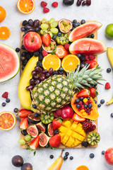 Healthy raw rainbow fruit platter background, mango papaya strawberries oranges blueberries pineapple watermelon on wooden board on light concrete background, top view, selective focus