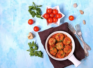 Fish meatballs in tomato sauce in a white ceramic pan on a light blue concrete background. Top view, copy space.