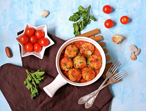 Fish meatballs in tomato sauce in a white ceramic pan on a light blue concrete background. Top view, copy space.