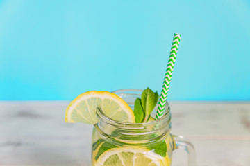 Mason jar glass of homemade lemonade with lemons, mint and paper straw on turquoise background. Summer refreshing beverage.