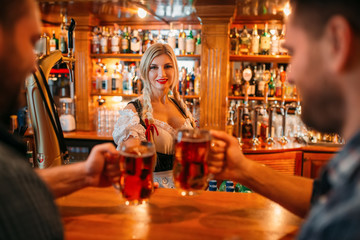 Two male friends clinking mugs with beer in pub