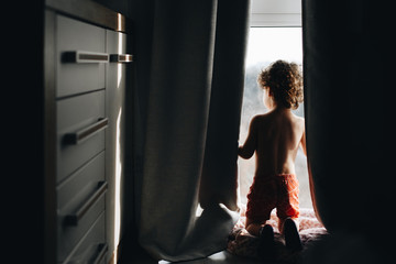 a little boy looks out the window in his parents ' room