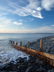 Beautiful beach scene with the groynes and pebbles lit up by the setting sunset at Westward Ho beach in Devon