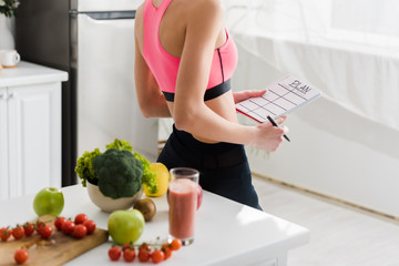 cropped view of woman in sportswear holding notebook with plan lettering in kitchen © LIGHTFIELD STUDIOS