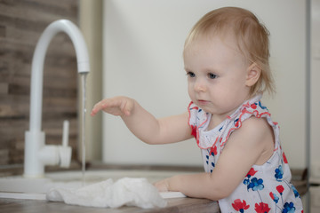Fototapeta premium cute little baby girl washing dishes in the home kitchen helping her mother with the housework and cleaning
