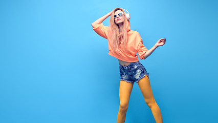 Young carefree DJ Girl jump Having Fun listen to music. Beautiful fashionable Woman smiling dance in trendy Outfit. Cheerful blond hipster in Stylish neon hoodie. Lifestyle enjoy music concept