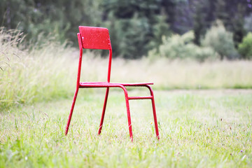 Red chair on green mown meadow in countryside.