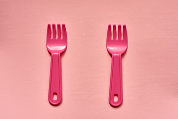 Close-up of two childish plastic pink forks on a pale pink background. Dishes for a picnic.