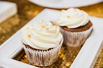 two brown cupcakes with white cream and golden sparkles