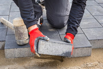 Hands of worker installing concrete paver blocks with rubber hammer