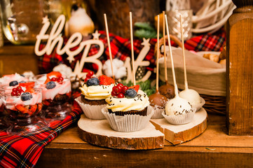 delicious cupcakes with berries and round candies on the wooden plate