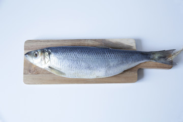 Fresh herring on a cutting wooden board on a white background with copy space for text. Flat lay. Top view.
