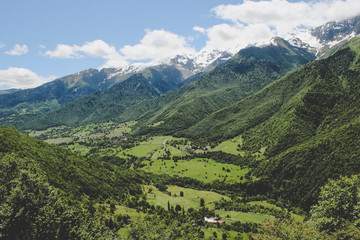 Fototapeta premium Scenic valley in the Caucasus Mountains with a small village, summer greens and snow-capped peaks