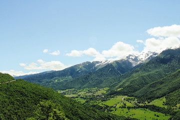 Scenic valley in the Caucasus Mountains with a small village, summer greens and snow-capped peaks