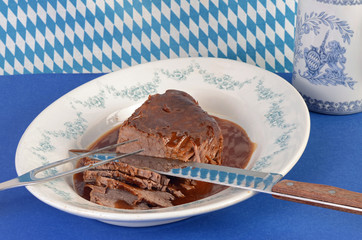 Sauerbraten in sauce on serving platter on blue and white colors of South Germany, Bavaria.