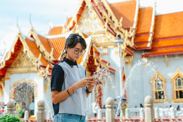 Asian woman traveler using smart phone reads and text message on her smart phone in the ancient temple scene background with copy space- Bangkok- Thailand