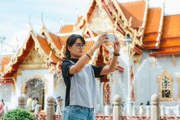 Asian woman traveler using smartphone take ancient temple photos in the ancient temple scene background with copy space- Bangkok- Thailand