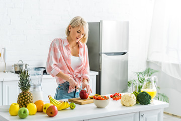 attractive young woman cutting apple near ingredients in kitchen