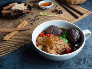 Close-up of Chinese chicken soup in a white cup decorated with Chinese shiitake mushrooms, goji berries, chicken blood and coriander leaves. Set on black wooden table and decoration.