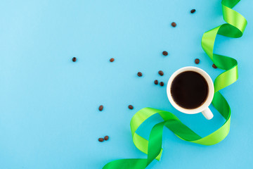 A cup of coffee with green silk ribbons and coffee beans on blue background. Design minimal concept. Mocup