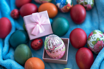 colorful Easter eggs of different sizes with a pink gift box on a blue blanket