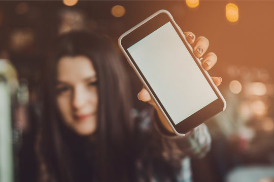 blurry portrait of a happy smiling brunette girl who holds a mobile phone with a clean screen ready for your logo or text..