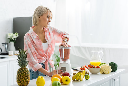 dreamy young woman preparing delicious smoothie in blender