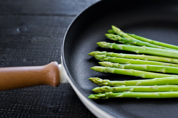 Fresh organic asparagus in a frying pan. Black background, top view, space for text.