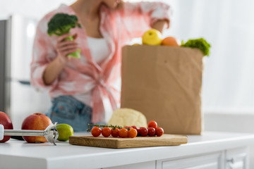 selective focus of chopping board with red cherry tomatoes near woman