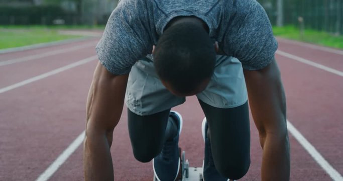Slow motion of young african male athlete is launching off the start line in a race in athletics stadium.