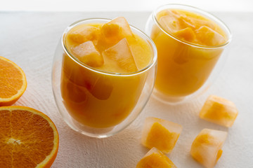 Orange Juice With Ice Cubes in Glasses Close Up. Ice Cubes With Small Pieces of Frozen Oranges