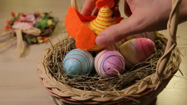 A woman is preparing for Easter, we see only her hands. A basket full of colorful eggs, a woman puts a toy chicken on top