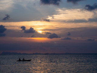 Silhouettes of people in a kayak in the rays of the setting sun against the background of clouds. Ko Phangan.Thailand.