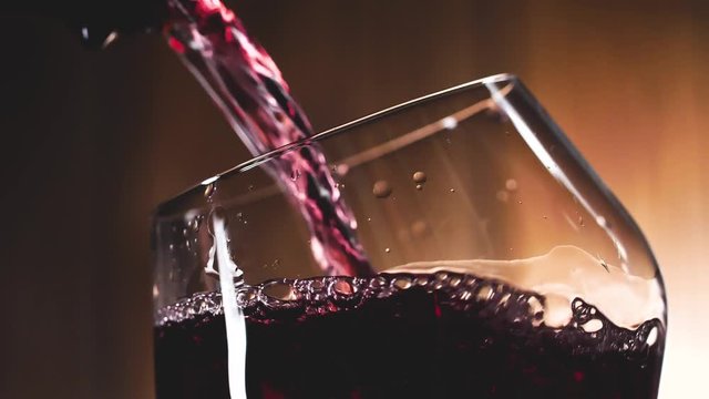 Wein. Rotwein, der in Weinglas &uuml;ber dunklem Hintergrund gie&szlig;t.