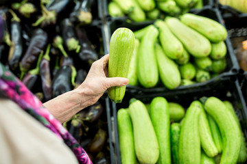 Grandma, the old woman chooses zucchini in the supermarket. hands