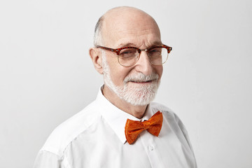 Maturity, people, aging and lifestyle concept. Isolated studio shot of friendly looking positive elderly mature European male in stylish glasses and orange bow tie going to theatre or special event