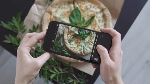 Woman hands taking photos of cheese pizza with basil by smartphone. Close up. Make photo of food with mobile phone camera