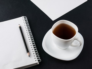 Office concept. Black pencil, blank notebook and white cup with coffee on black and white paper background. Top view. Copy space