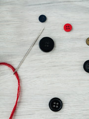 All for needlework: Buttons, a needle with a red thread, tangle of thread on a wooden gray table. Top view. Copy space