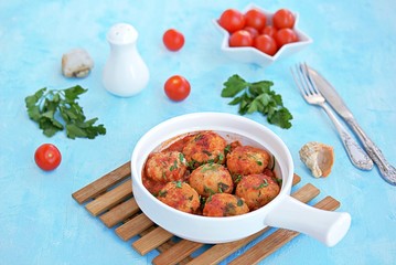 Fish meatballs in tomato sauce in a white ceramic pan on a light blue concrete background