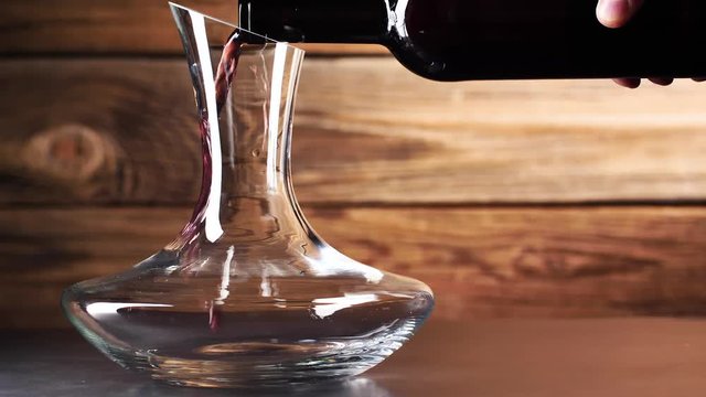 Wein. Rotwein, der in Weinglas &uuml;ber dunklem Hintergrund gie&szlig;t.