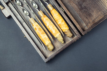 Close up handles Big luxury stainless steel skewers set in wooden box for grill and barbecue. Expensive high quality exclusive gift for man hunter. Male present background