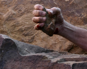 A Single Hand Holding a Small Rough Textured Stone, Showing Pressure to the  Fingers and Thumb, with Part Shown Forearm on a Blurred Rock Background.