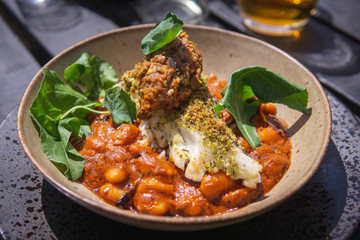 A cooked white fish fillet served on beans in a tomato sauce with green leaves