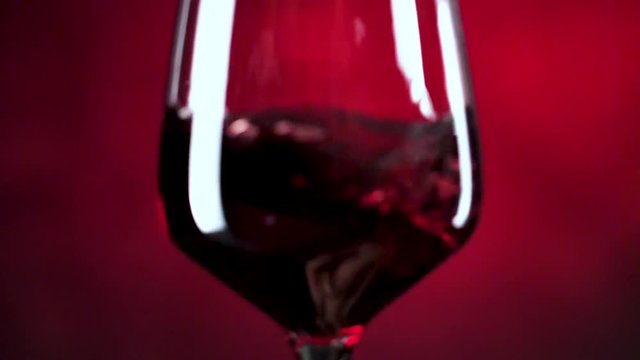 Wein. Rotwein, der in Weinglas &uuml;ber dunklem Hintergrund gie&szlig;t.