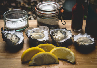 Fresh oysters served on a wooden board with salt, pepper, lemons and hot sauce