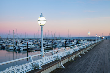 A wooden pier at sunset looking over the marina at the sailboats and yachts