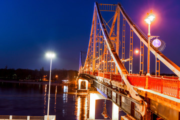 Pedestrian metal bridge with colored lights across the river