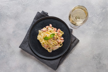 Pasta with trout and cream in dark plate and a glass of white wine on light background. Delicious Mediterranean lunch.
